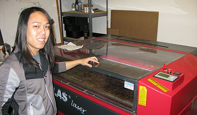 Christian Fernandez stands in front of “Smaug” (named for the dragon from Lord of the Rings), an 80-watt laser cutter that Ace Monster Toys imported from China. (Photo by Daniel McGlynn)