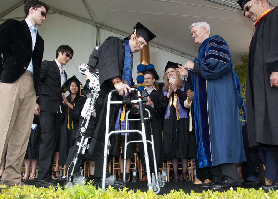 Austin Whitney crossing the stage at commencement with a bionic exoskeleton