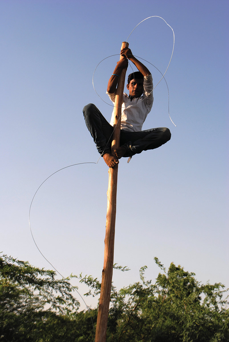 Man climbing pole while carrying wire