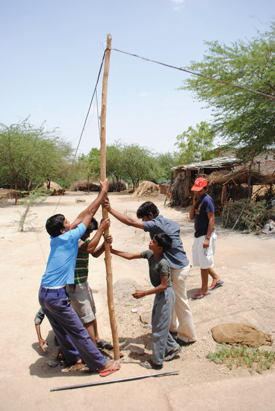 Villagers raising pole with wire