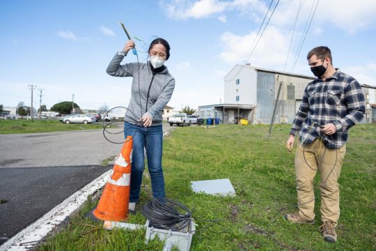 Graduate students check on fiber optic cables installed beneath a paved road at Richmond Field Station