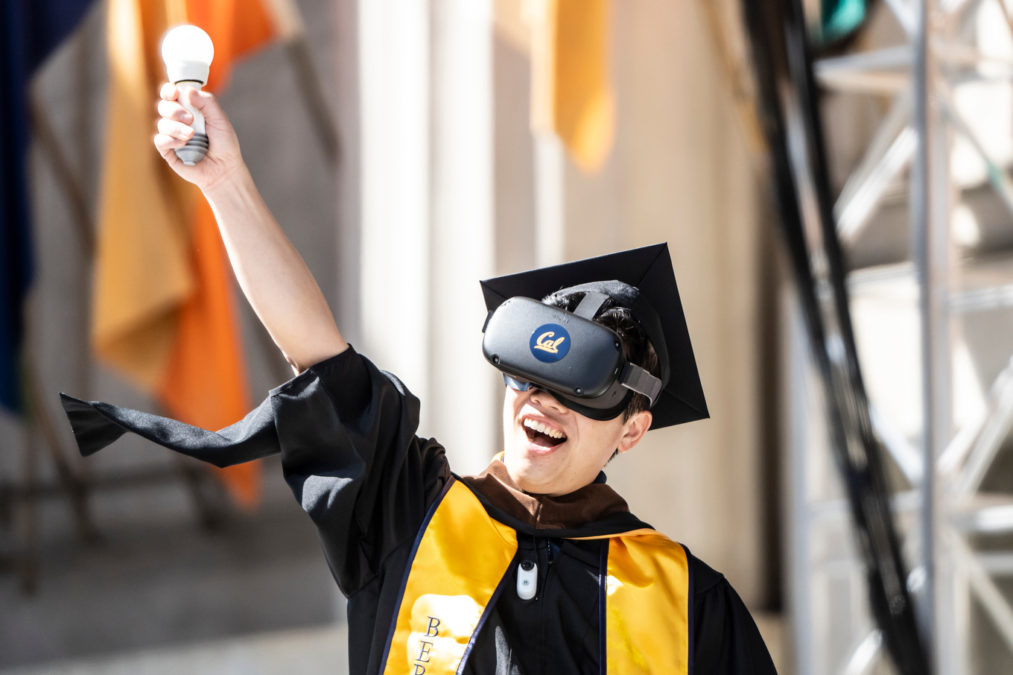 Graduate crosses the stage with VR goggles in the Greek Theatre