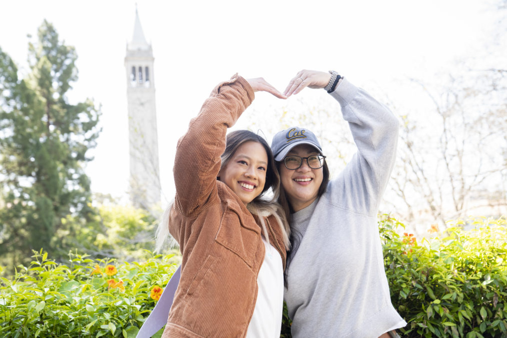 Two students making a heart with their arms on Cal Day 2022 with the campanile in the background.