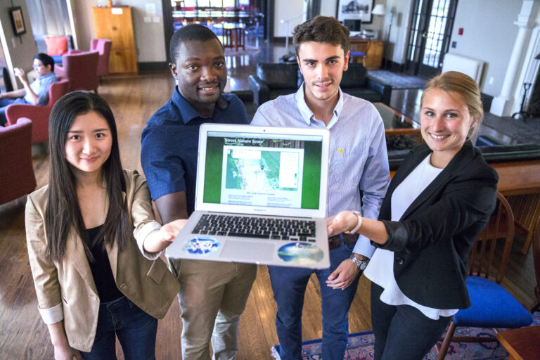 Four MBA students holding up a laptop computer