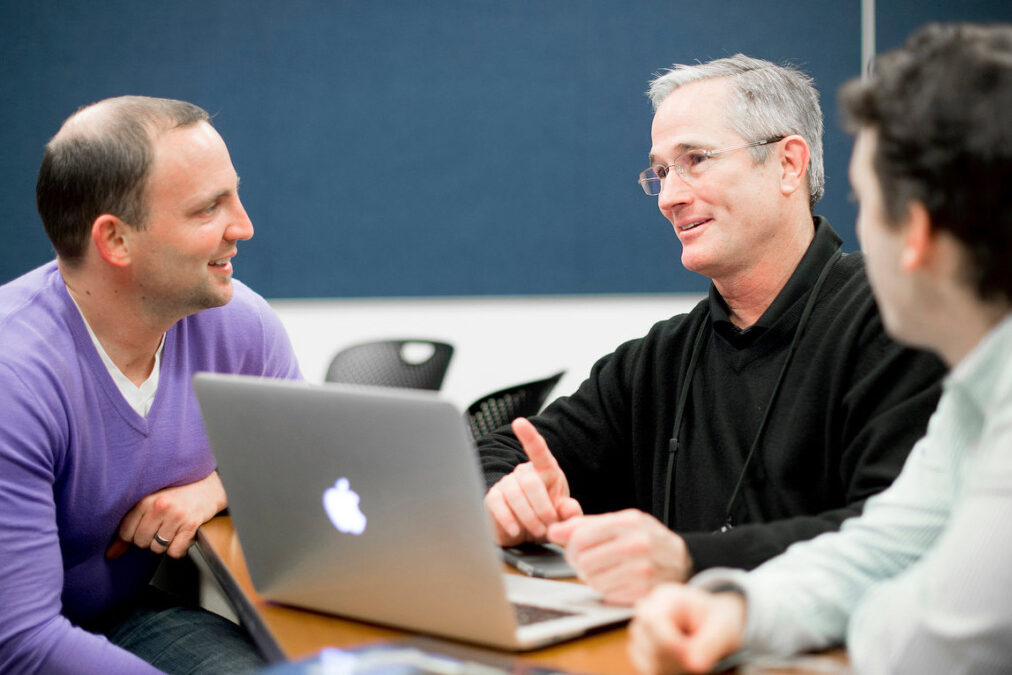 Men talking around laptop in executive education class