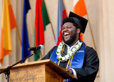 Student in a black cap and gown speaking at a podium at commencement