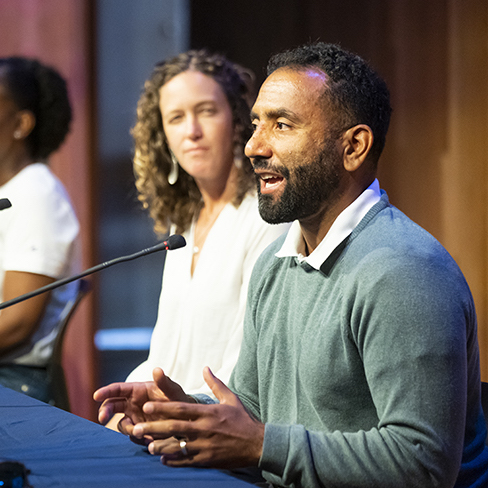 Aaron Streets, right, speaking into a microphone at a panel.
