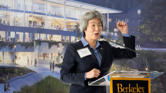 Dean Liu stands at a lectern while holding up her left fist in a cheer.