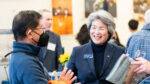 Dean Liu smiles as she listens to a guest wearing a mask at a college event.