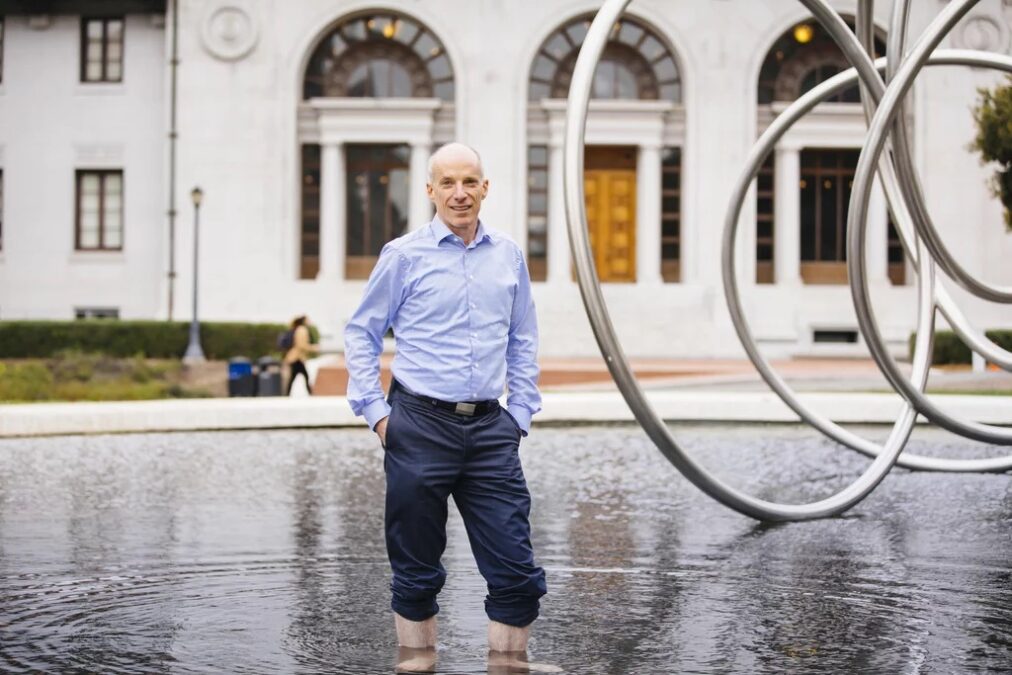 David Sedlak stands in the Mining Circle fountain next to the sculpture with his pants rolled up above the water.
