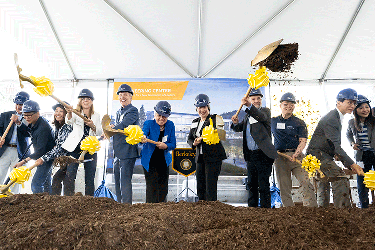 People in hardhats shovel dirt in the air at a groundbreaking ceremony.