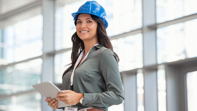Photo of female engineer wearing hard hat and holding a tablet.