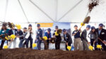 People in hard hats shoveling dirt for the ceremonial groundbreaking