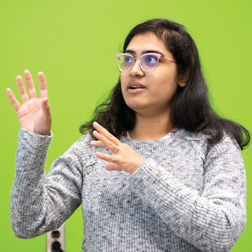 Female student making hand signs in front of green wall