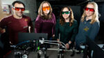 (from left) UC Berkeley professors Hillel Adesnik, Laura Waller, and Rikky Muller, and UC Berkeley graduate student Liz Murray pose in Waller’s lab with a prototype of their neurotechnology for two-way communication with the brain.