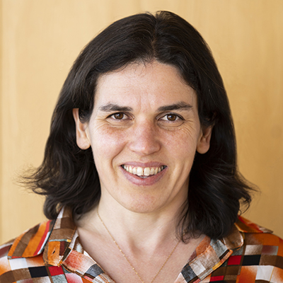 Headshot of Alexia Aubault wearing an orange, black and white patterend-shirt in front of a tan background