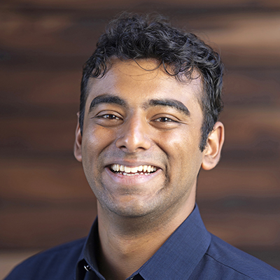 Headshot photo of Abhinav Subramaniam smiling at the camera in front of a blurred brown background