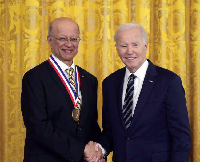 Ashol Gadgil, wearing the National Medal of Technology and Innovation, shakes hands with President Joe Biden in front of a gold curtain.