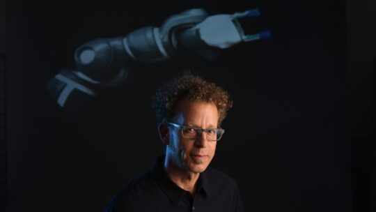 Ken Goldberg photographed next to a robot arm. (Photo Copyright Noah Berger / 2017)