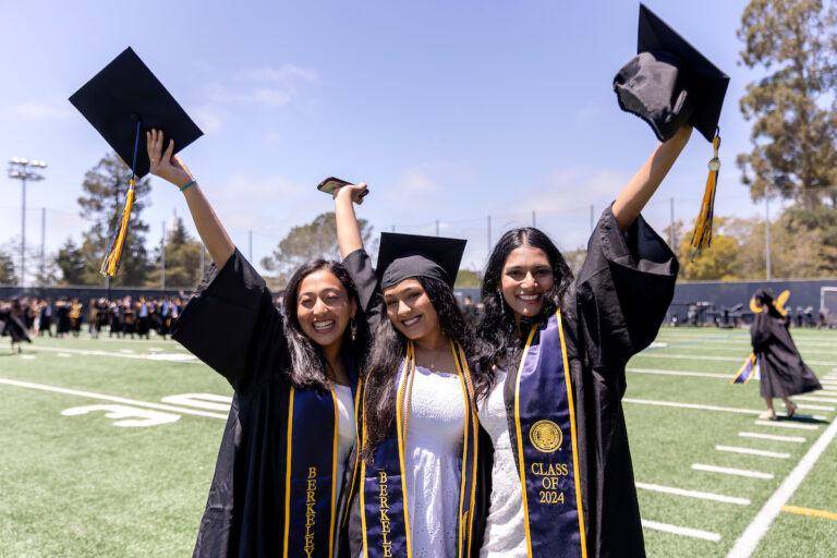 Three graduates hold up their cap 