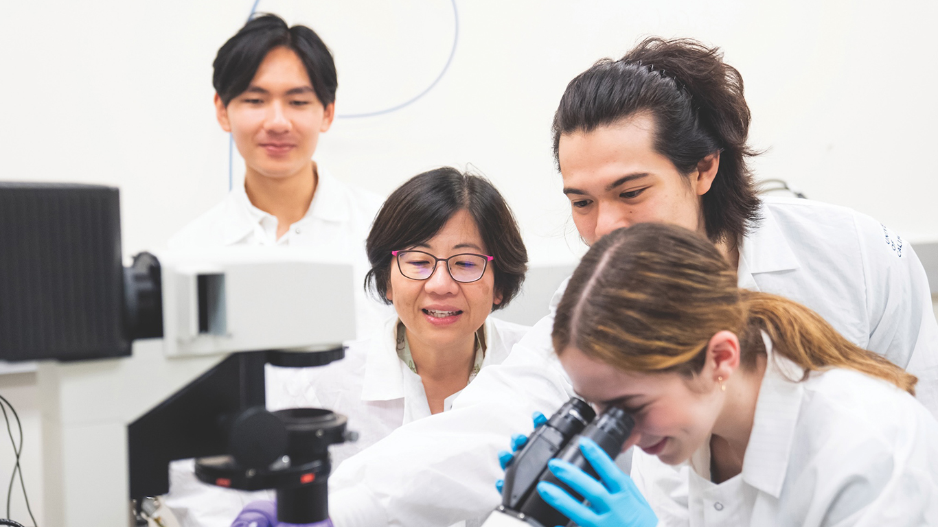 Students using a microscope as a professor and two other students look on