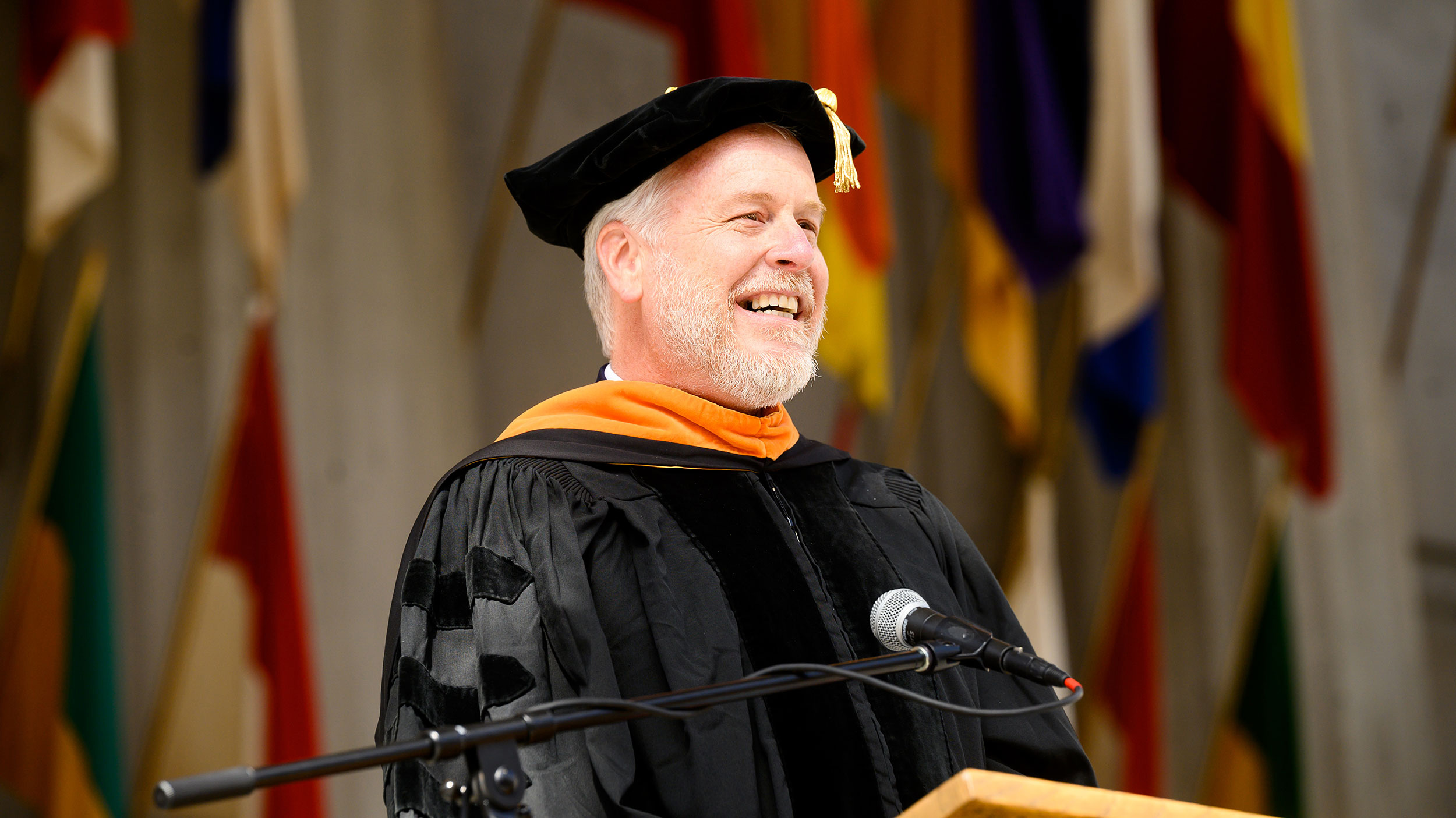 Mark Asta is at the podium of Berkeley Engineering's commencement ceremony, wearing regalia.