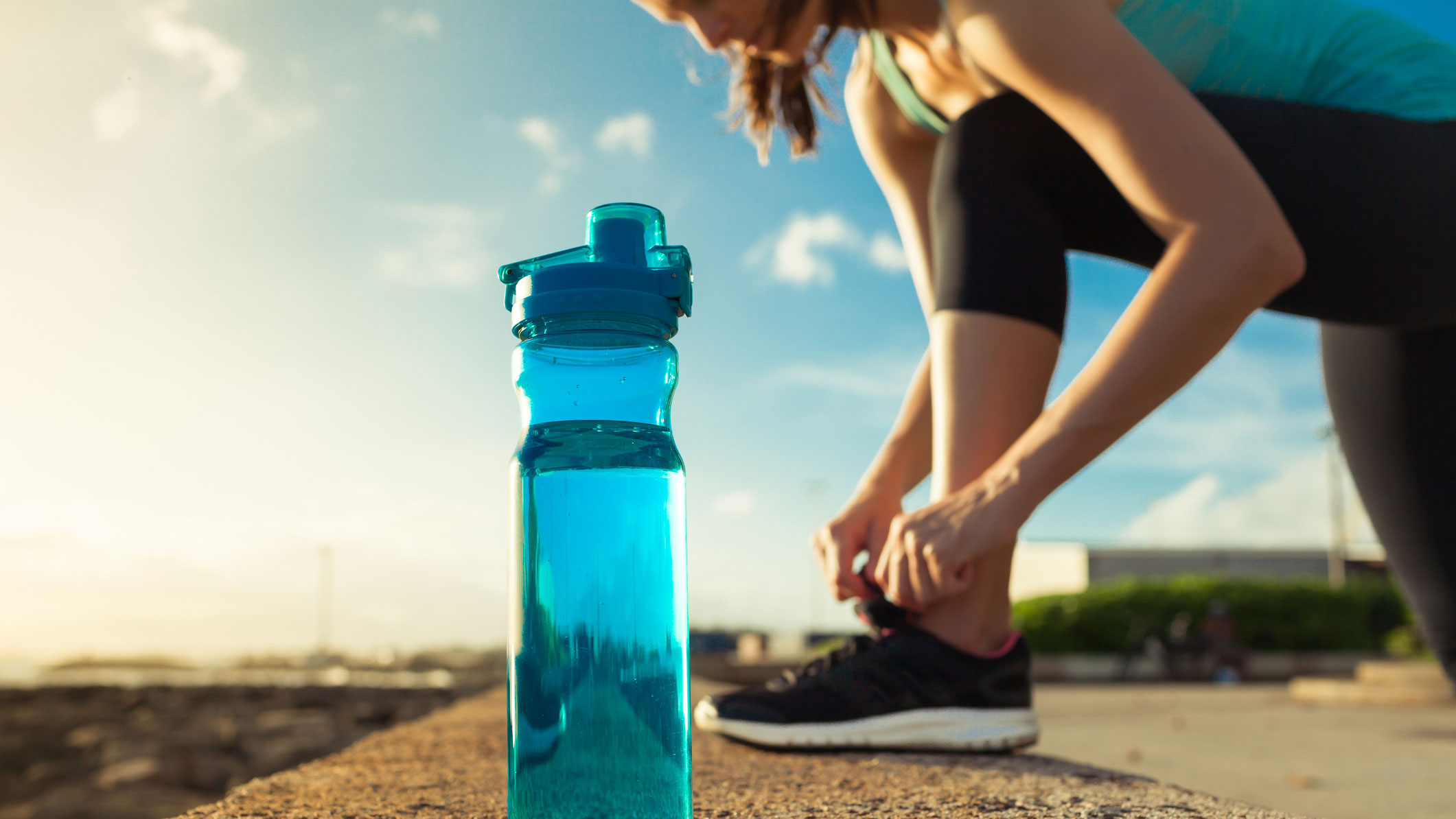 Runner tying her shoe next to a bottle of water.