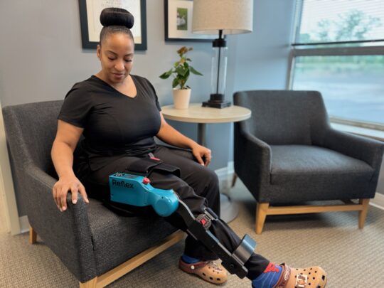 Woman seated and wearing Reflex robotic device on her leg.