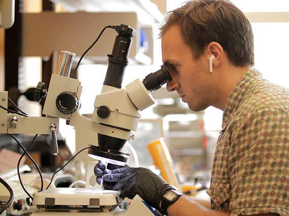 Graduate student Daniel Drew uses a microscope to assemble a tiny ionocraft